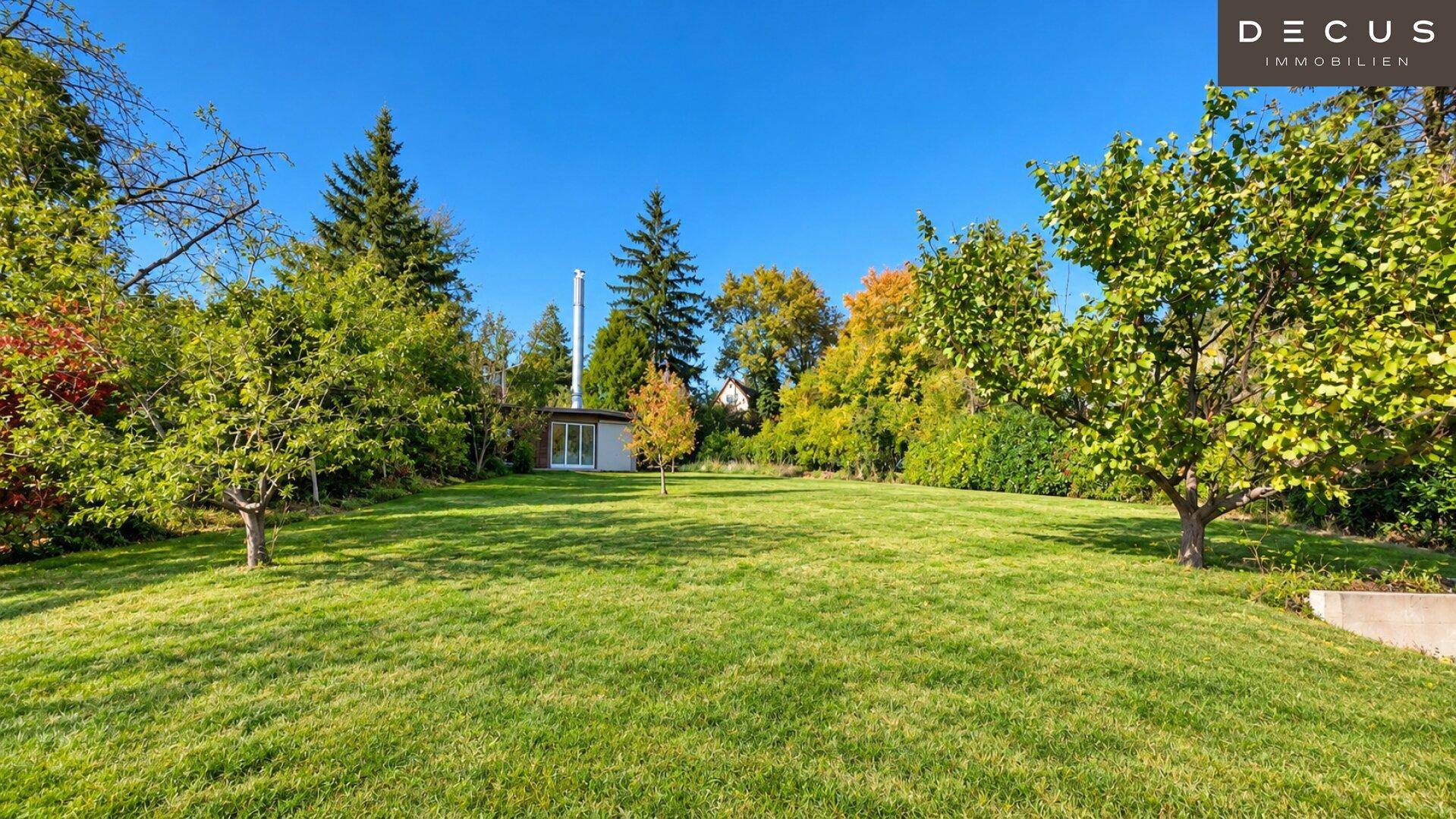 Weitläufige Rasenfläche mit Bäumen und einem kleinen Gartenhaus im Hintergrund der Landschaft.