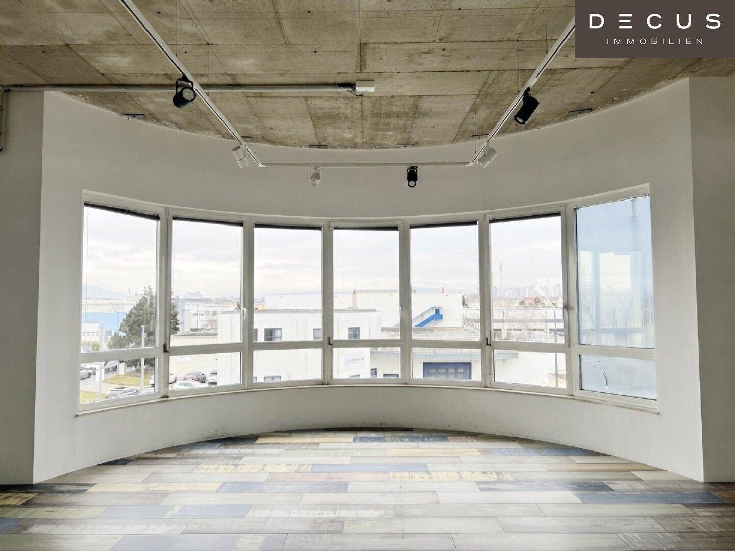Heller Büroraum mit gebogener Fensterfront, die viel Tageslicht hereinlässt und eine weite Aussicht bietet.