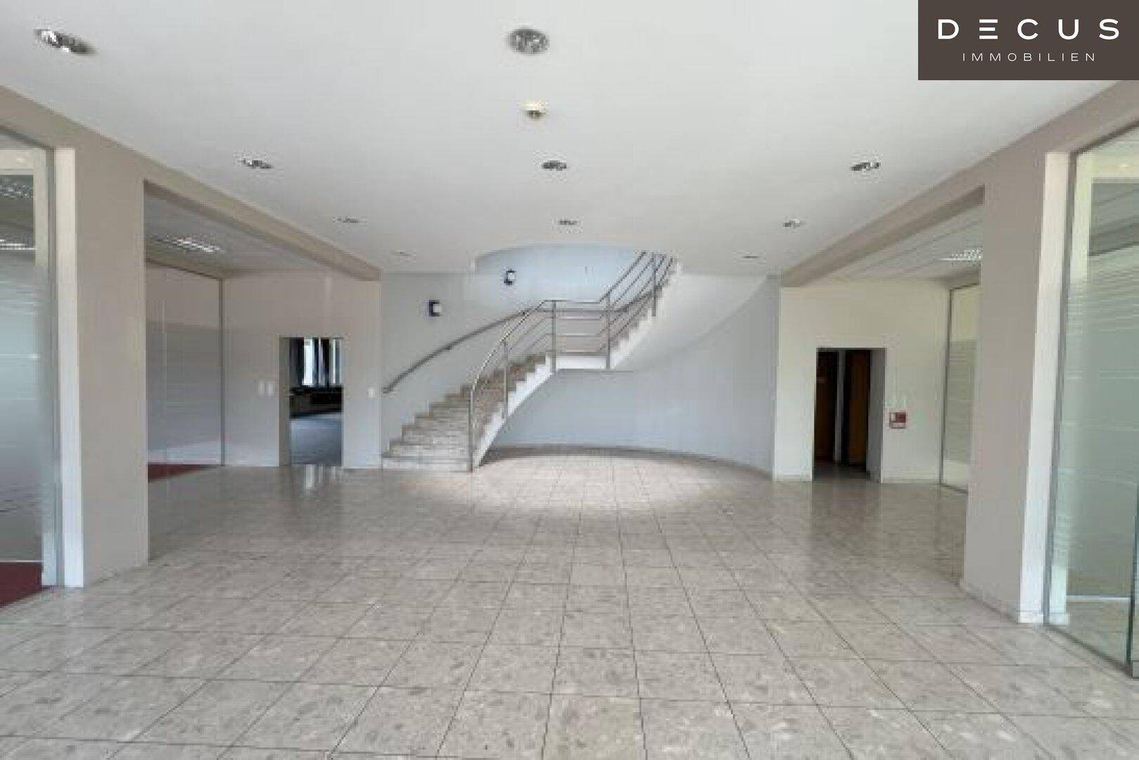 Geräumige Eingangshalle mit Marmorfliesen, einer geschwungenen Treppe und viel Tageslicht.