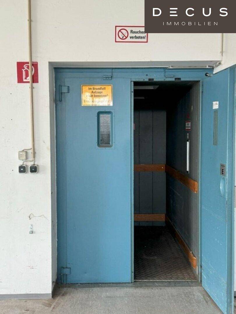 Großer Lastenaufzug mit blauen Türen und Warnhinweisen, bereit für den Transport von Gütern.