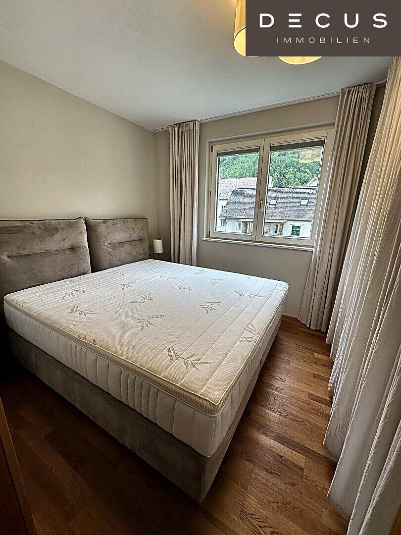 Gemütliches Schlafzimmer mit Doppelbett, Holzboden und Blick ins Grüne durch das Fenster.