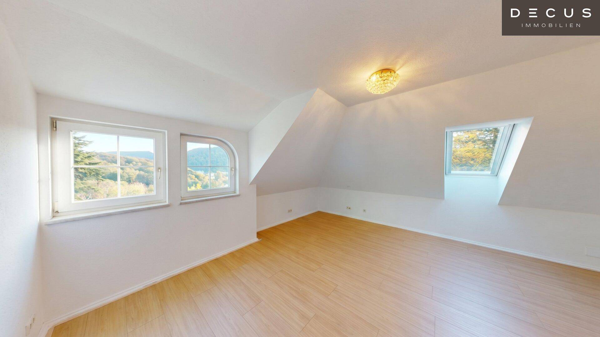 Helles Dachzimmer mit Holzboden, Dachfenster und Blick auf die umliegende Landschaft.