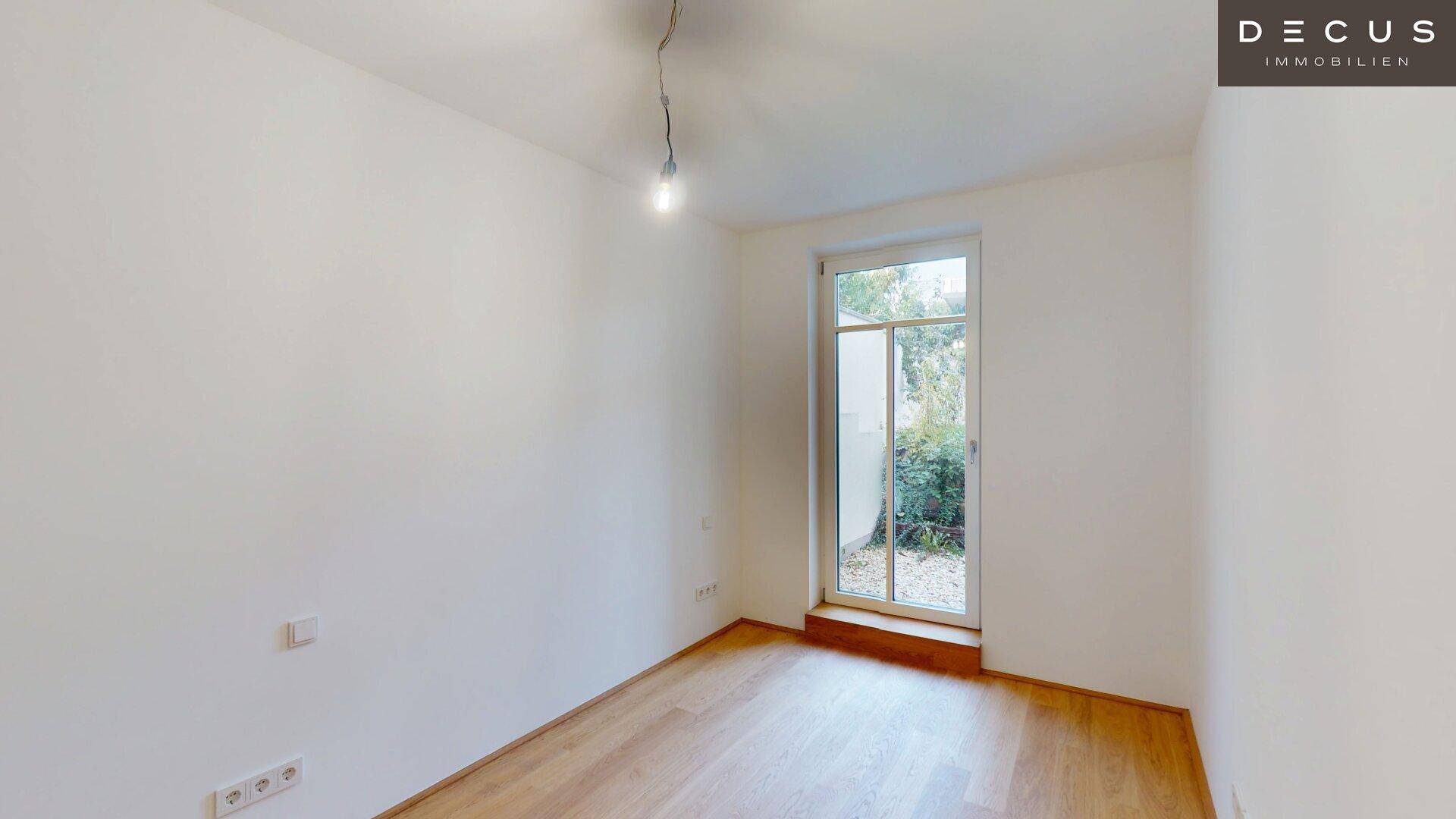 Helles Zimmer mit Holzboden und großem Fenster mit Blick ins Grüne.