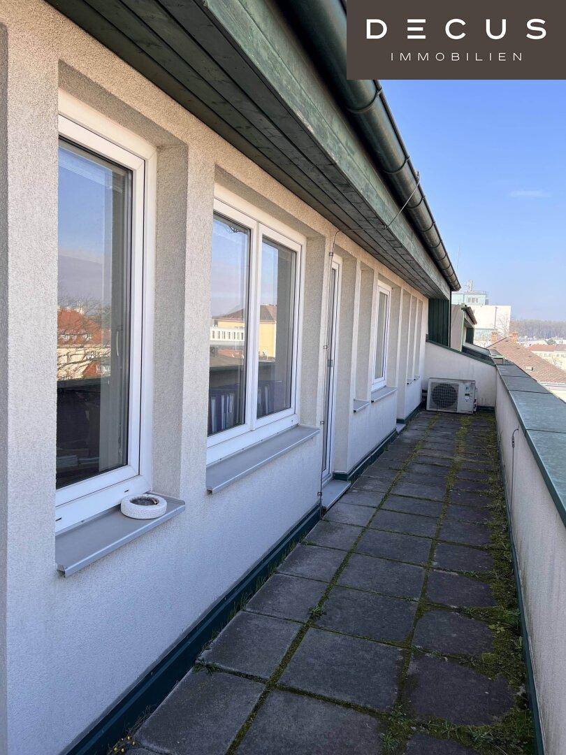 Langer Balkon mit Steinplattenboden und einer Klimaanlage, bietet einen Blick auf die Stadt.