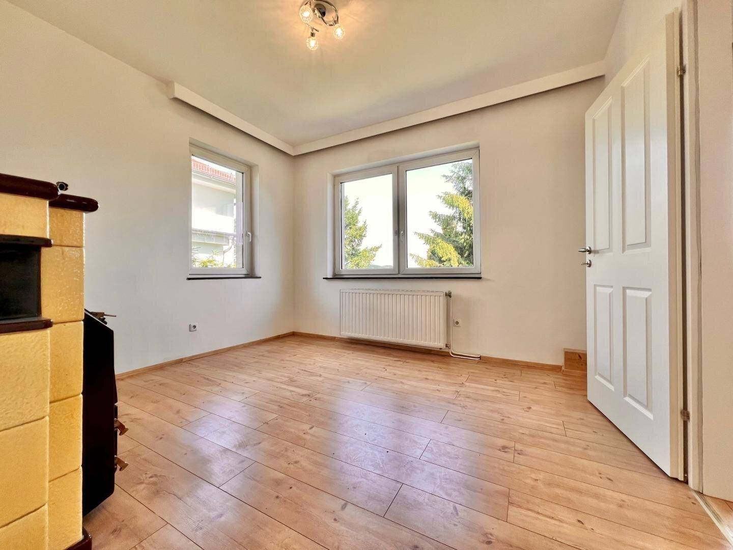 Helles Zimmer mit Holzfußboden, Heizkörper und einem traditionellen Kachelofen, ideal als Wohnraum.