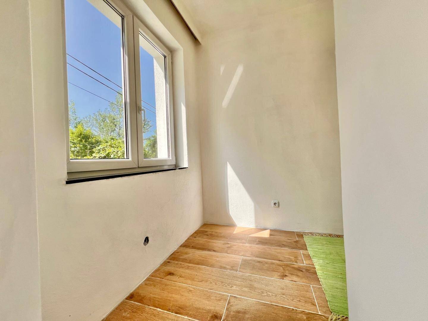 Kleines, helles Zimmer mit Holzboden und einem Fenster mit Blick ins Freie, ideal als Arbeits- oder Gästezimmer.