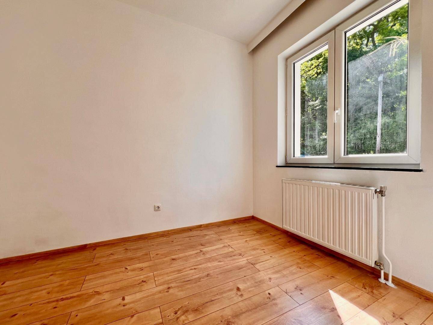 Helles Zimmer mit Holzboden und einem großen Fenster, das viel Sonnenlicht bietet und eine angenehme Atmosphäre schafft.