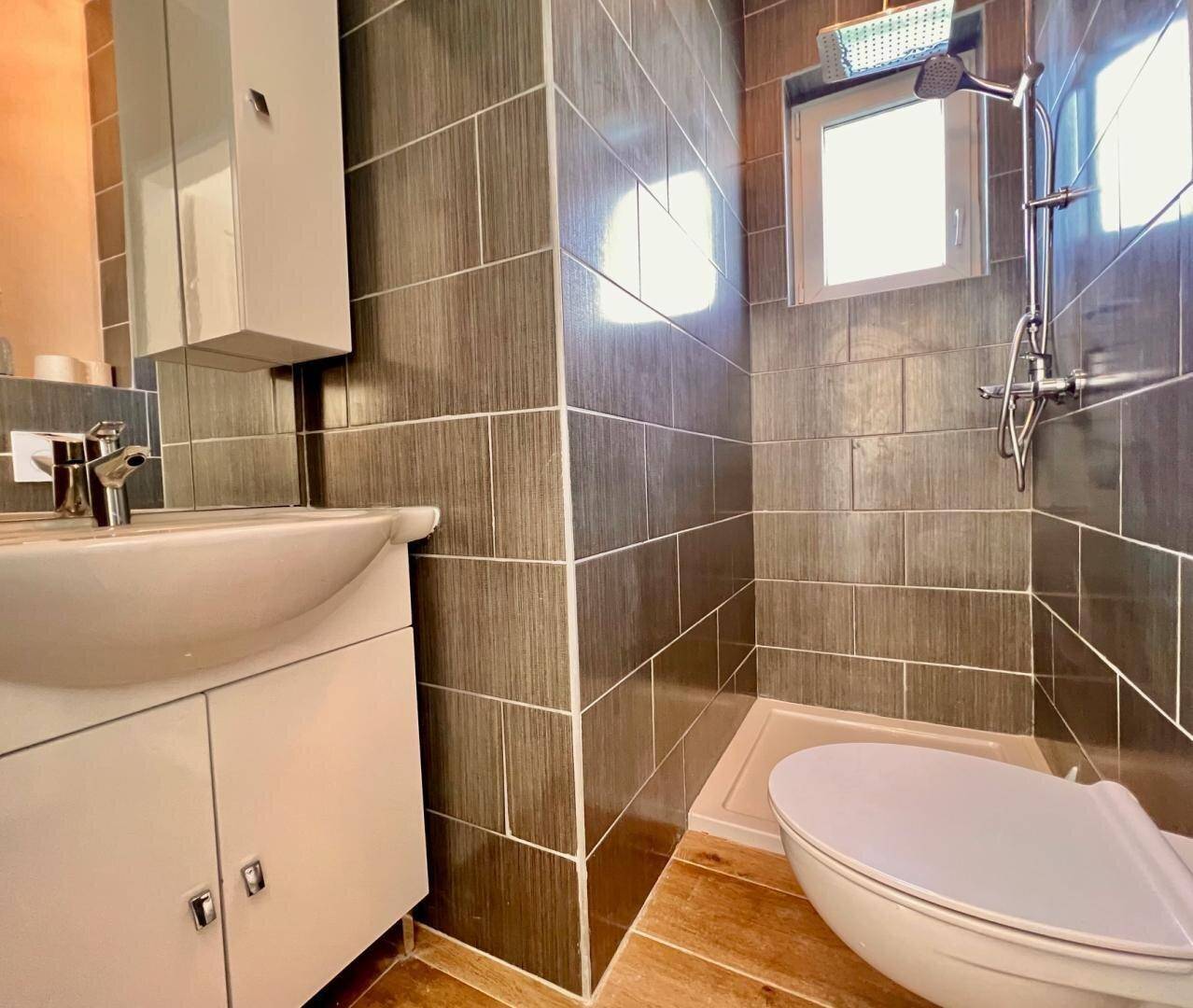 Modernes Badezimmer mit dunklen Fliesen, Dusche, Waschbecken und Spiegelschrank, in gutem Zustand.