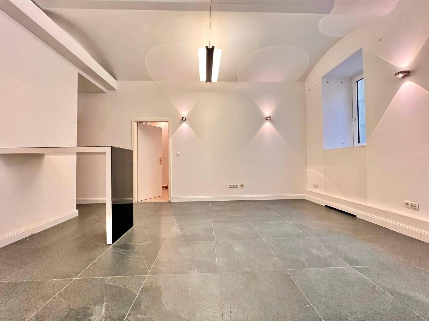 Heller Raum mit dunklem Fliesenboden, gewölbter Decke und modernen Wandleuchten.