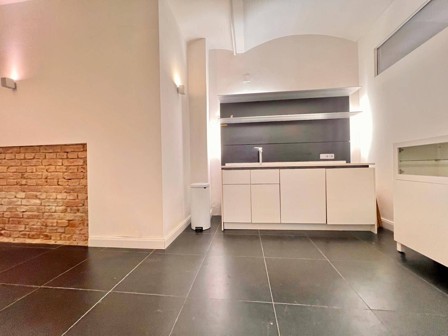 Küchenzeile mit weißen Schränken, dunkler Arbeitsplatte und Spüle, ergänzt durch eine freiliegende Ziegelwand.