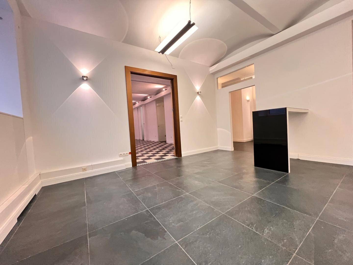 Geräumiger Raum mit dunklem Fliesenboden, gewölbter Decke und modernen Wandleuchten.