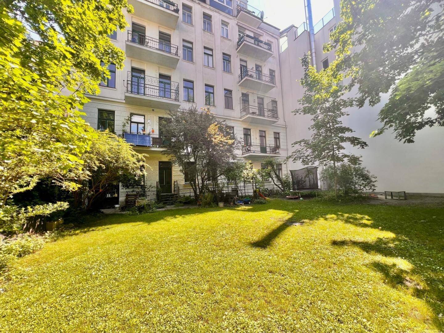 Grüner Gemeinschaftsgarten mit Rasenfläche und Bäumen hinter einem Mehrfamilienhaus.