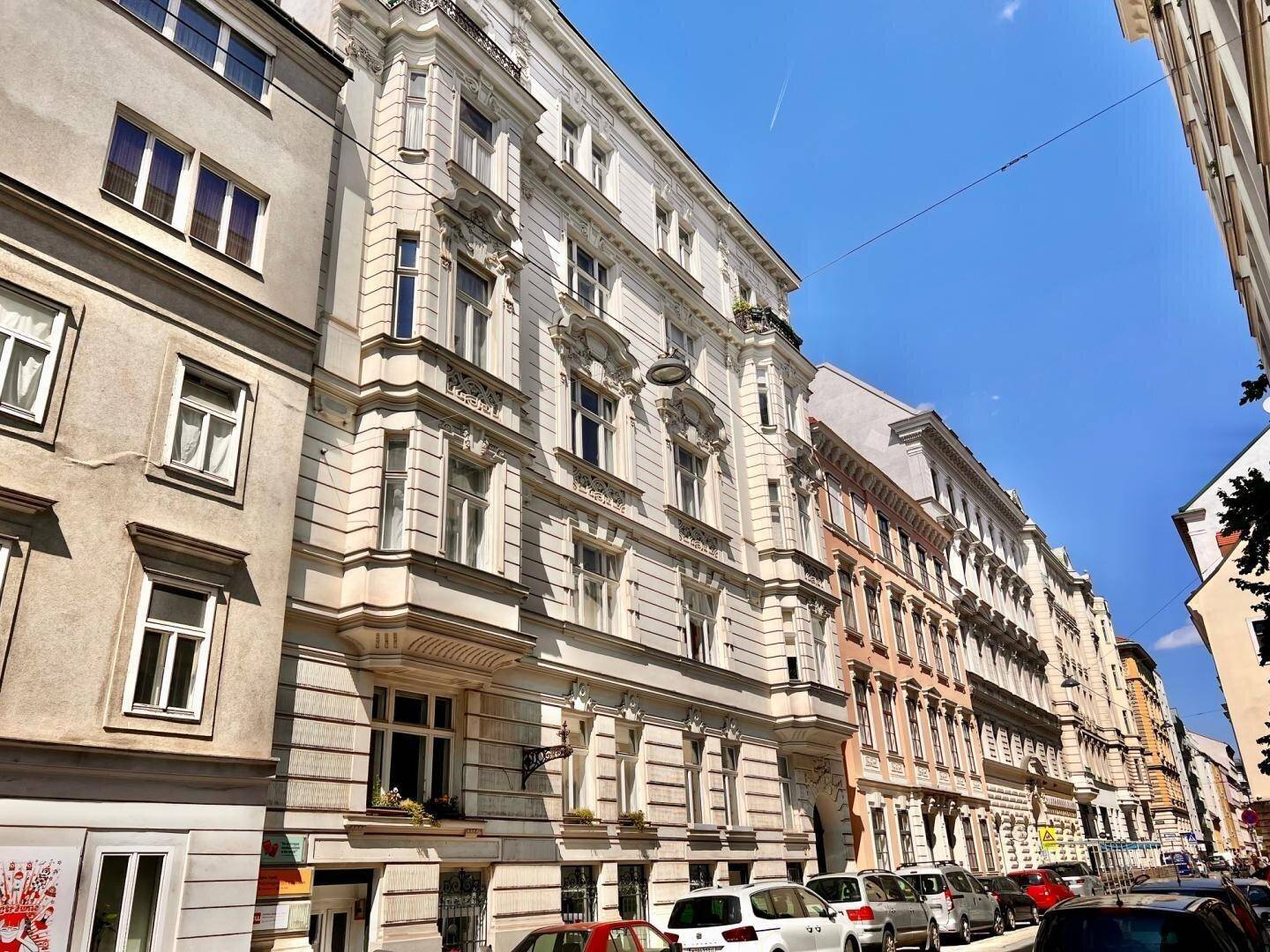 Historisches Gebäude mit reich verzierter Fassade und klassischen Balkonen an einer belebten Straße.