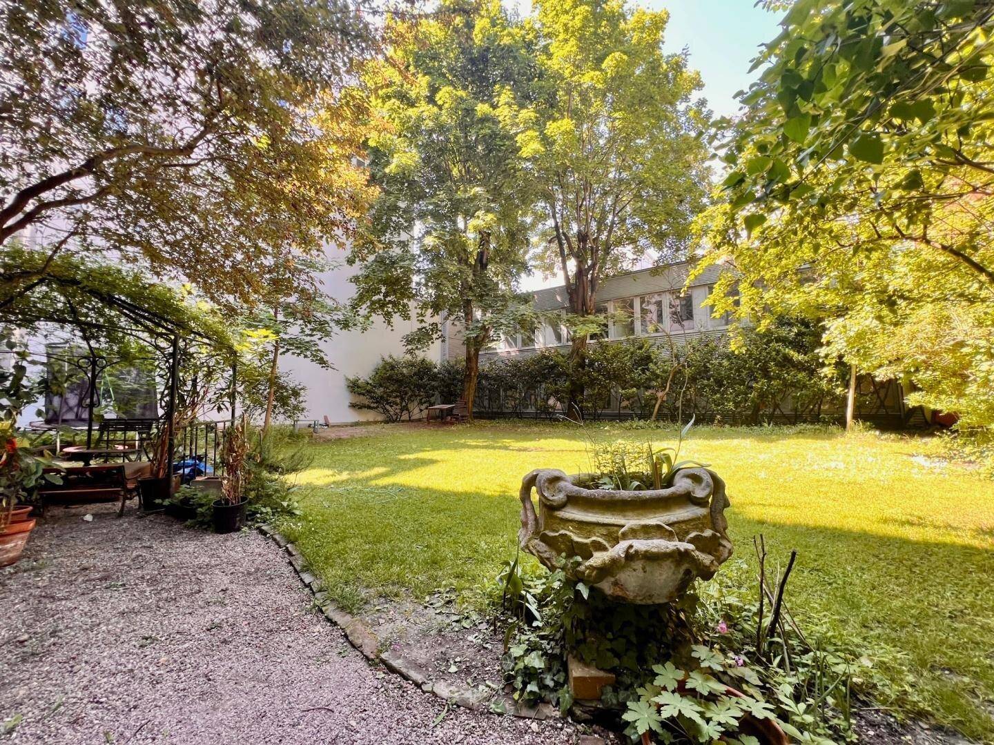Idyllischer Gemeinschaftsgarten mit Rasen, alten Bäumen und einem dekorativen Steinbrunnen.