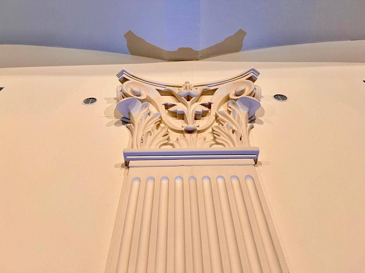 Nahaufnahme eines verzierten Kapitells an einer Säule, das die klassische Architektur des Raumes unterstreicht.