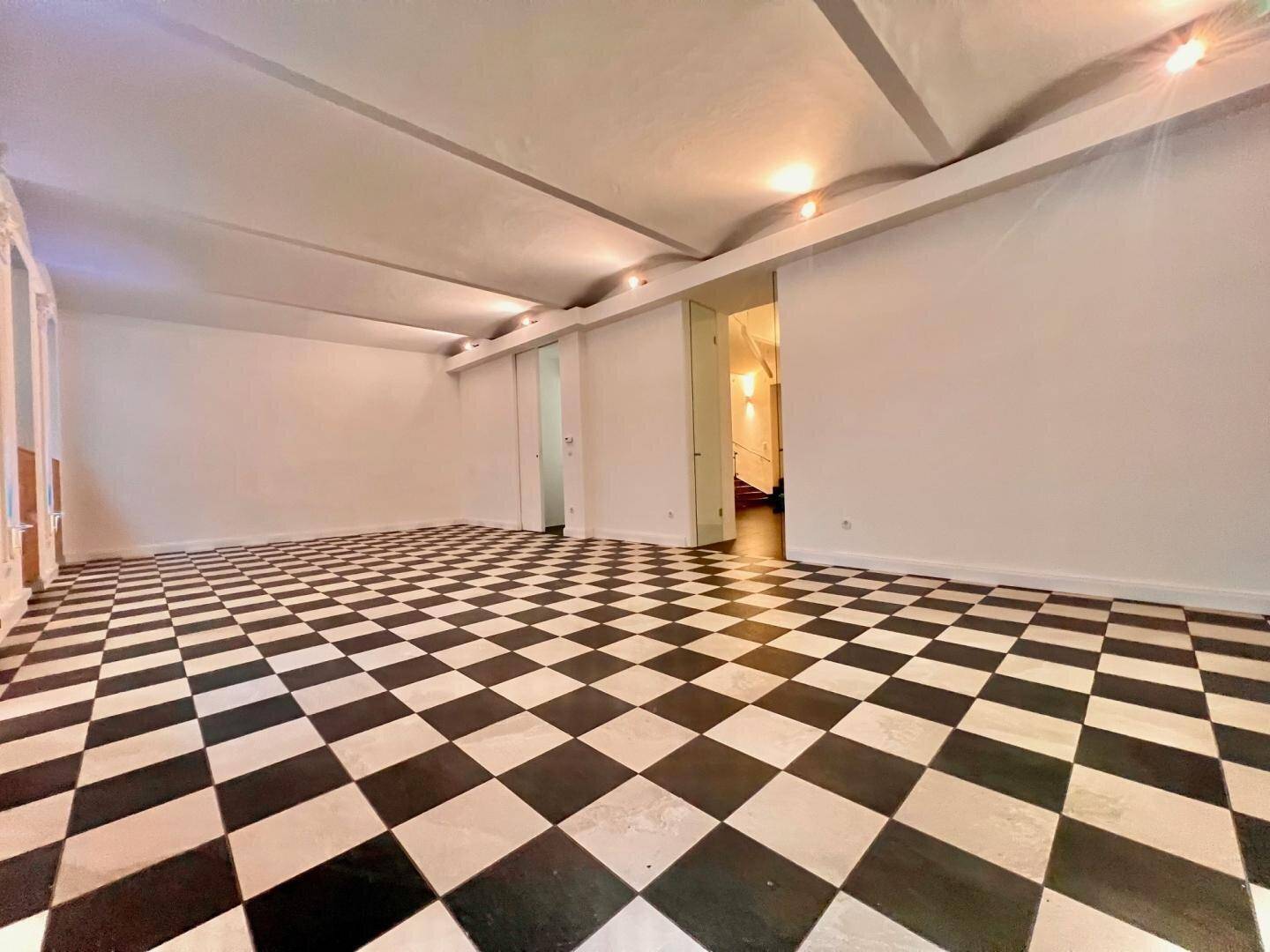 Weitläufiger Raum mit schwarz-weißem Fliesenboden, hohen Decken und indirekter Beleuchtung.