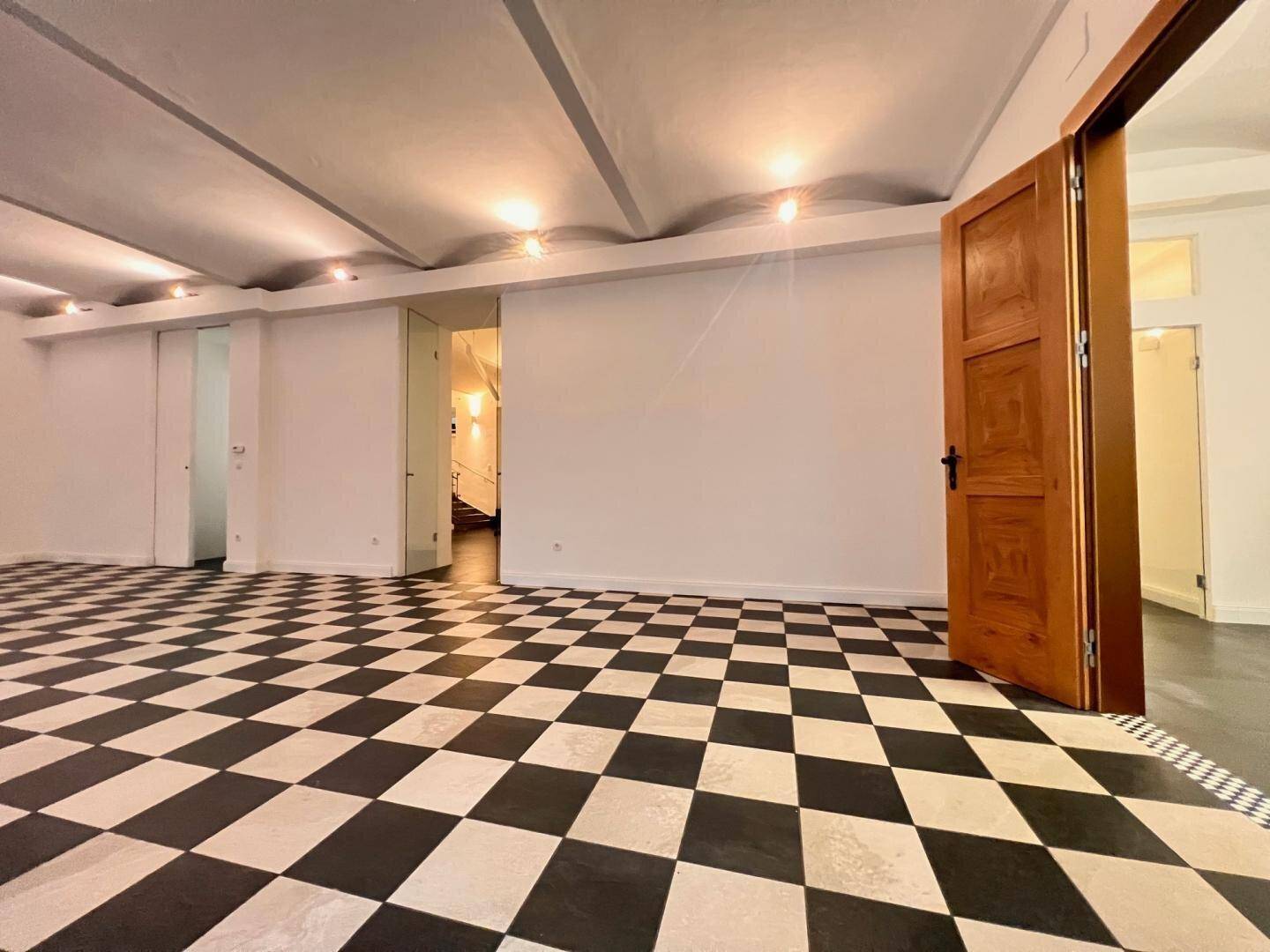 Geräumiger Innenraum mit markantem Schachbrettmuster-Boden, hohen Decken und eleganten Holztüren.