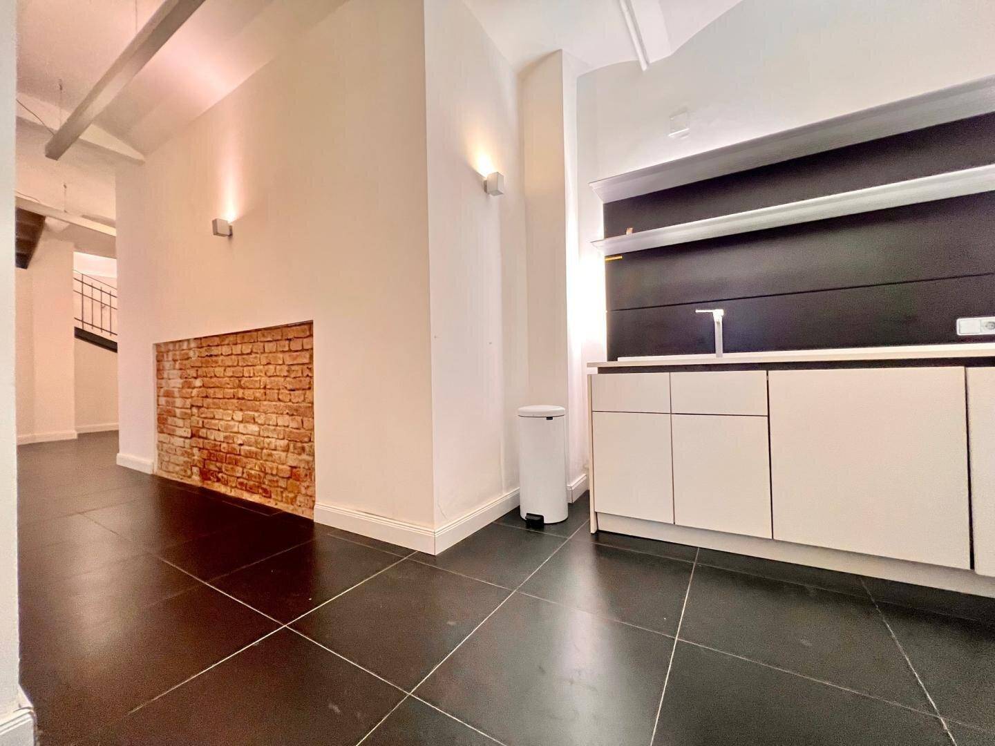 Moderne Küchenzeile mit weißen Schränken, dunkler Rückwand und freigelegter Ziegelwand.