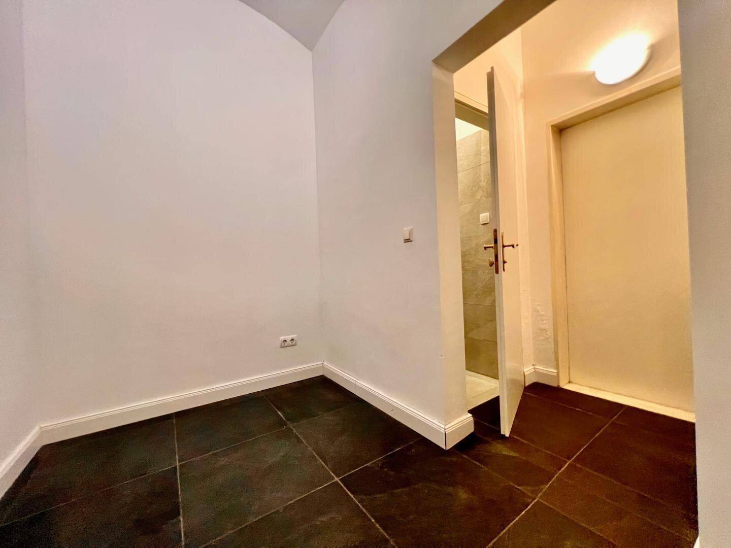 Kleiner Raum mit dunklem Fliesenboden und Zugang zu einem weiteren Bereich.