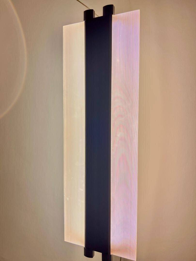 Vertikale, moderne Lichtinstallation mit farbigen Akzenten an einer hellen Wand.