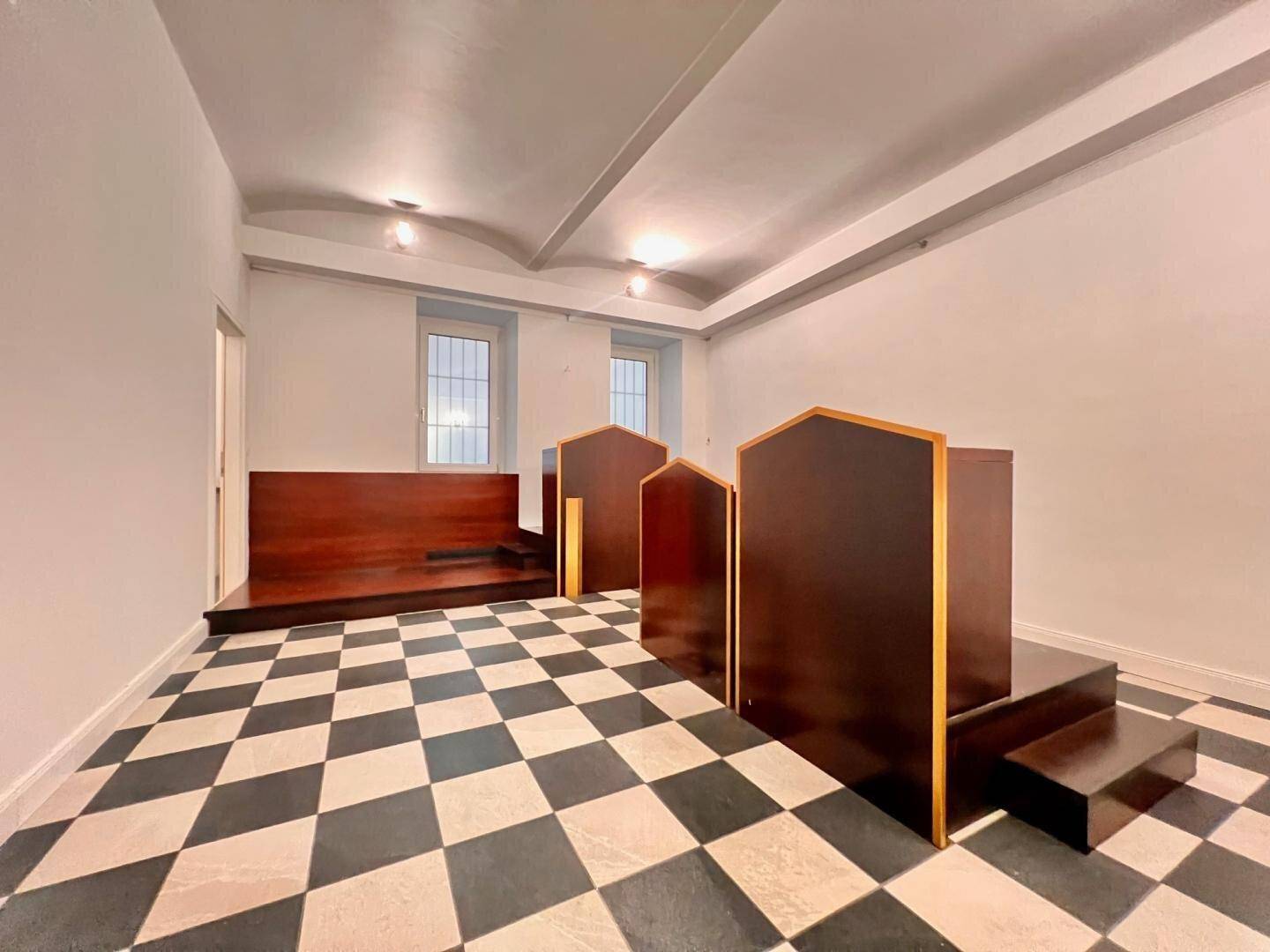 Großer Raum mit markantem Schachbrettmuster-Boden und erhöhten Holzpodesten für vielseitige Nutzung.