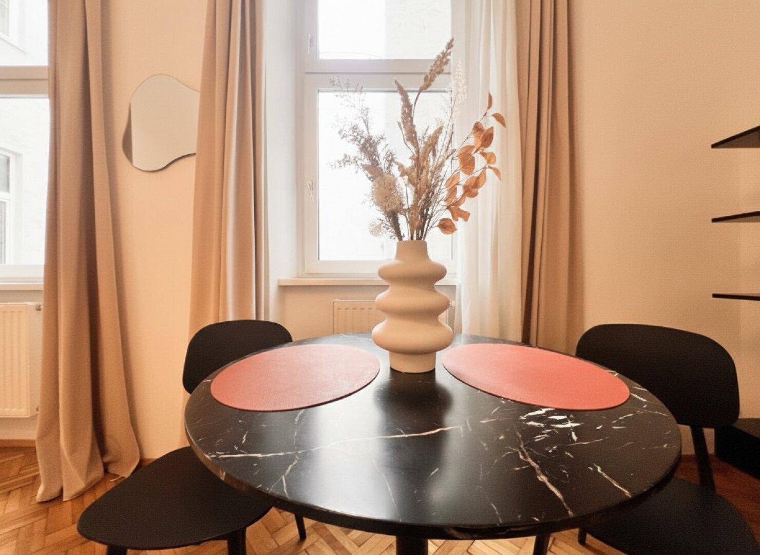 Moderner Esstisch mit schwarzer Marmorplatte und stilvoller Dekoration am Fenster.