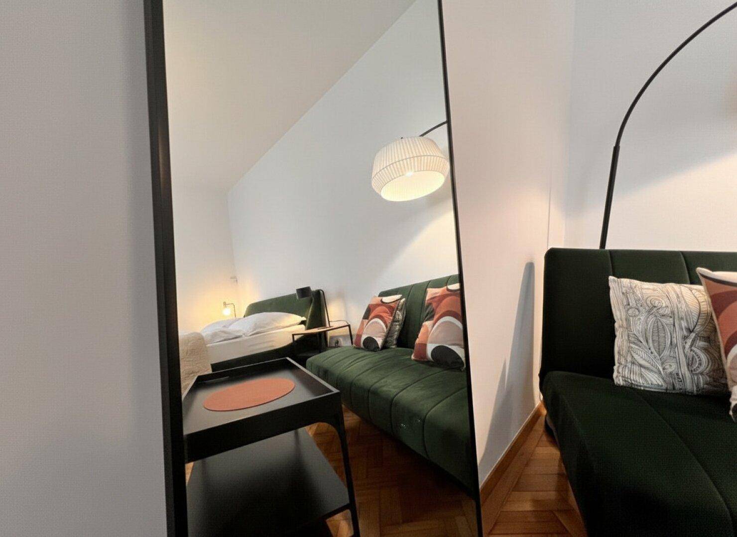 Spiegelreflexion des modernen Studio-Apartments mit Sofa und Bettbereich.