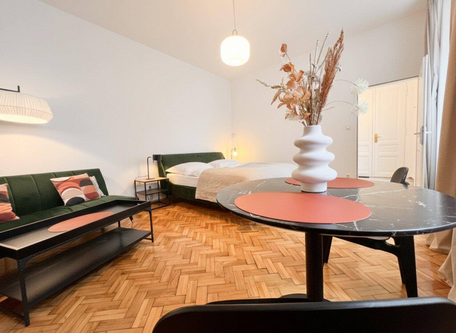 Heller Wohnbereich mit Parkettboden, grünem Sofa und einem dekorativen Esstisch.