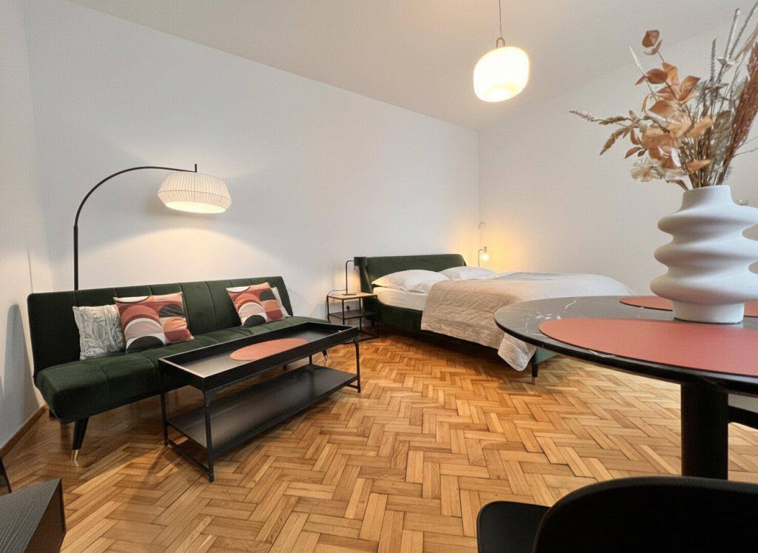 Geräumiges Studio-Apartment mit Parkettboden, bequemer Sitzecke und Schlafbereich.