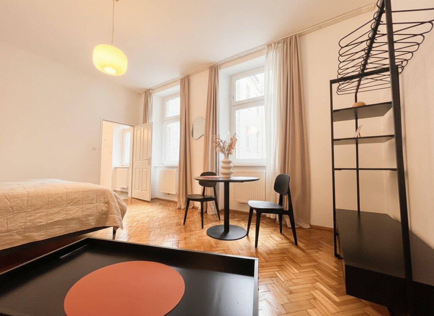 Studio-Apartment mit Parkettboden, großen Fenstern und offenem Kleiderständer.