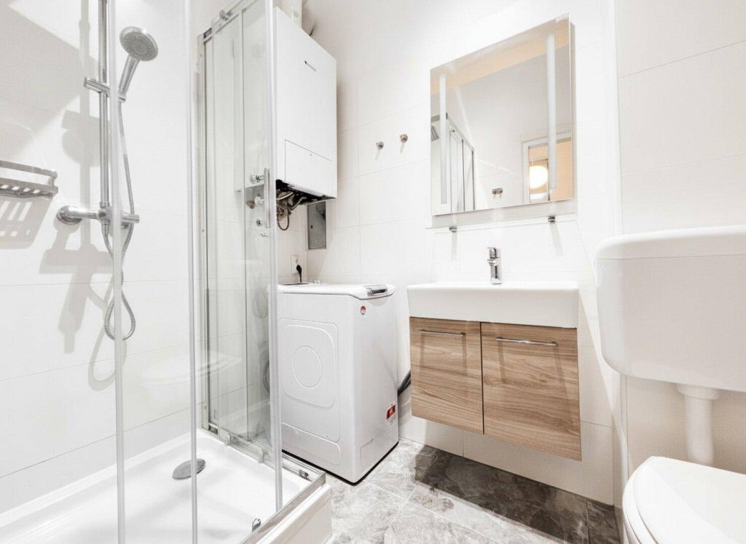 Modernes Badezimmer mit Dusche, Waschbecken und Waschmaschine in weißem Design.