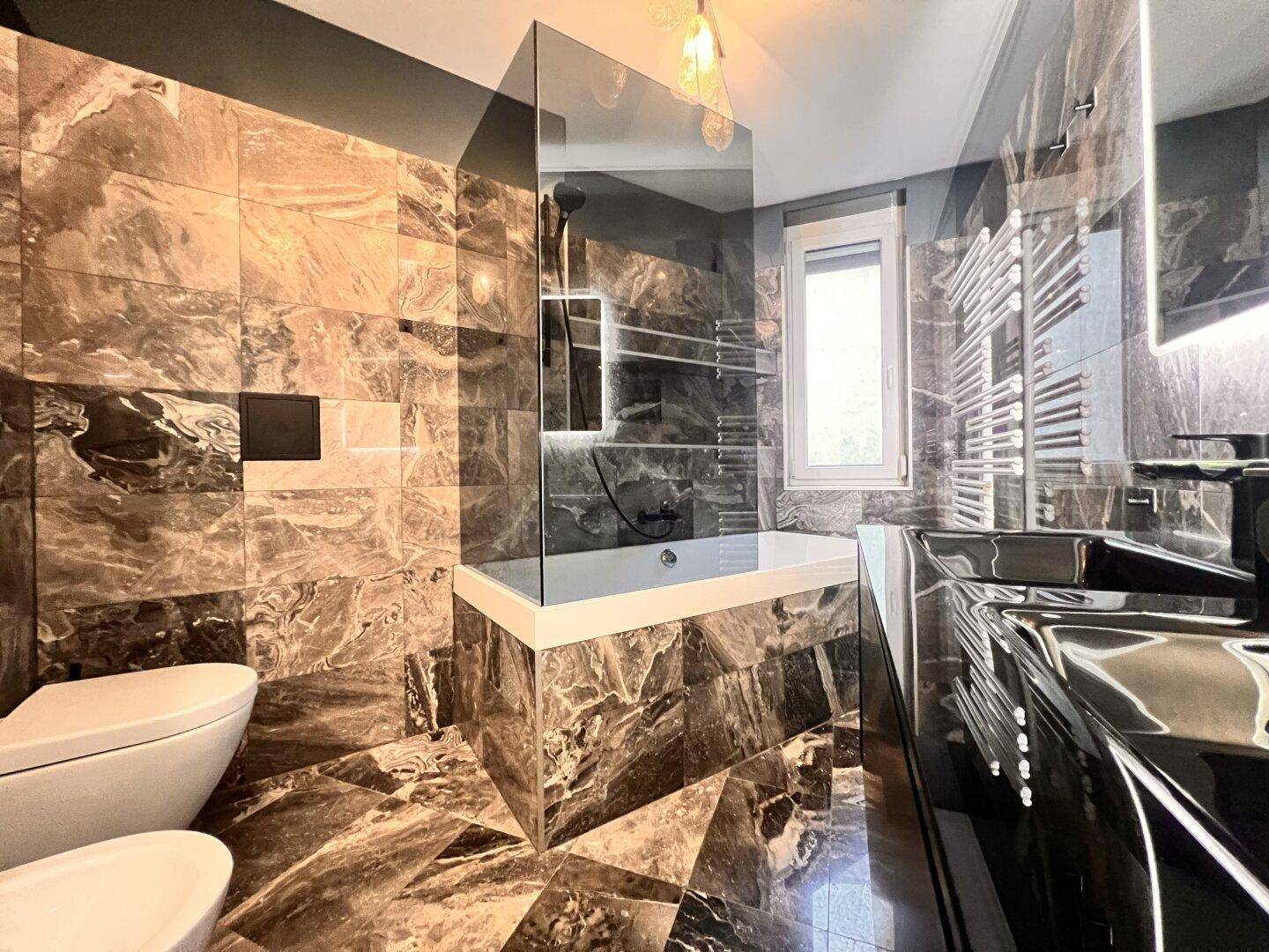 Modernes Badezimmer mit dunklen Marmorfliesen, Badewanne und integrierter Dusche.