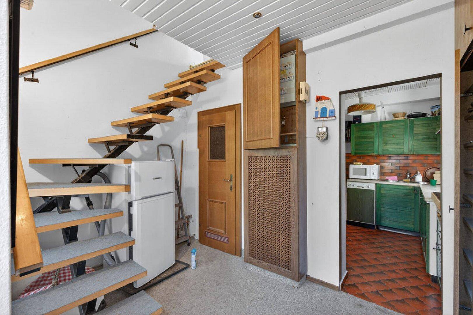 Eingangsbereich mit offener Treppe und Blick in die Küche mit grünen Schränken.