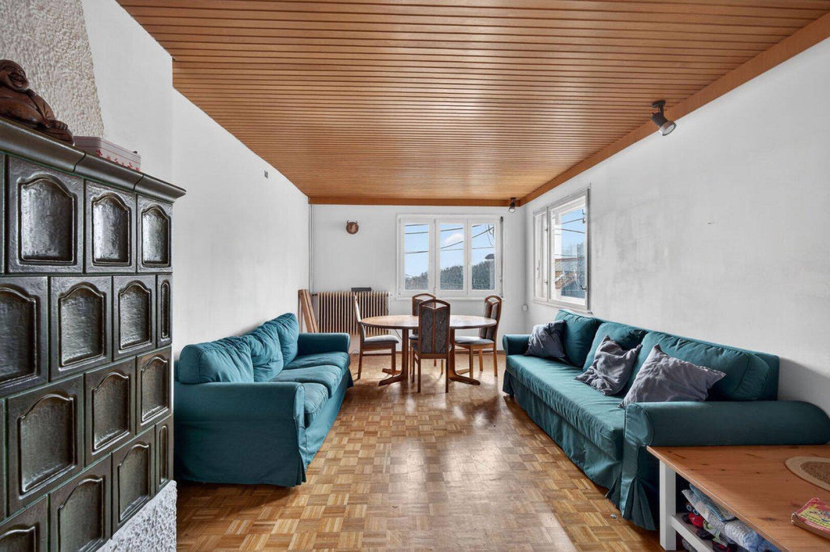 Gemütliches Wohnzimmer mit Kachelofen, Holzdecke und Parkettboden.