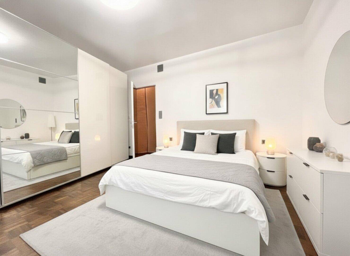 Gemütliches Schlafzimmer mit weißem Interieur, Parkettboden und großem Spiegelkleiderschrank.