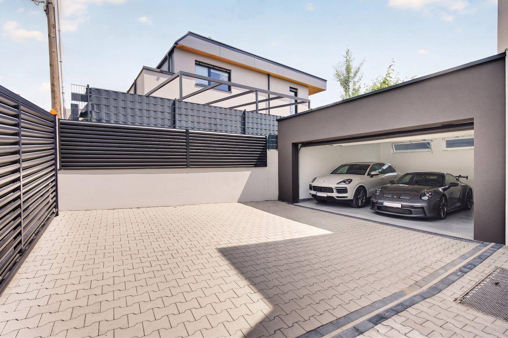 Geräumige Doppelgarage mit zwei Luxusautos und gepflasterter Zufahrt vor dem modernen Haus.