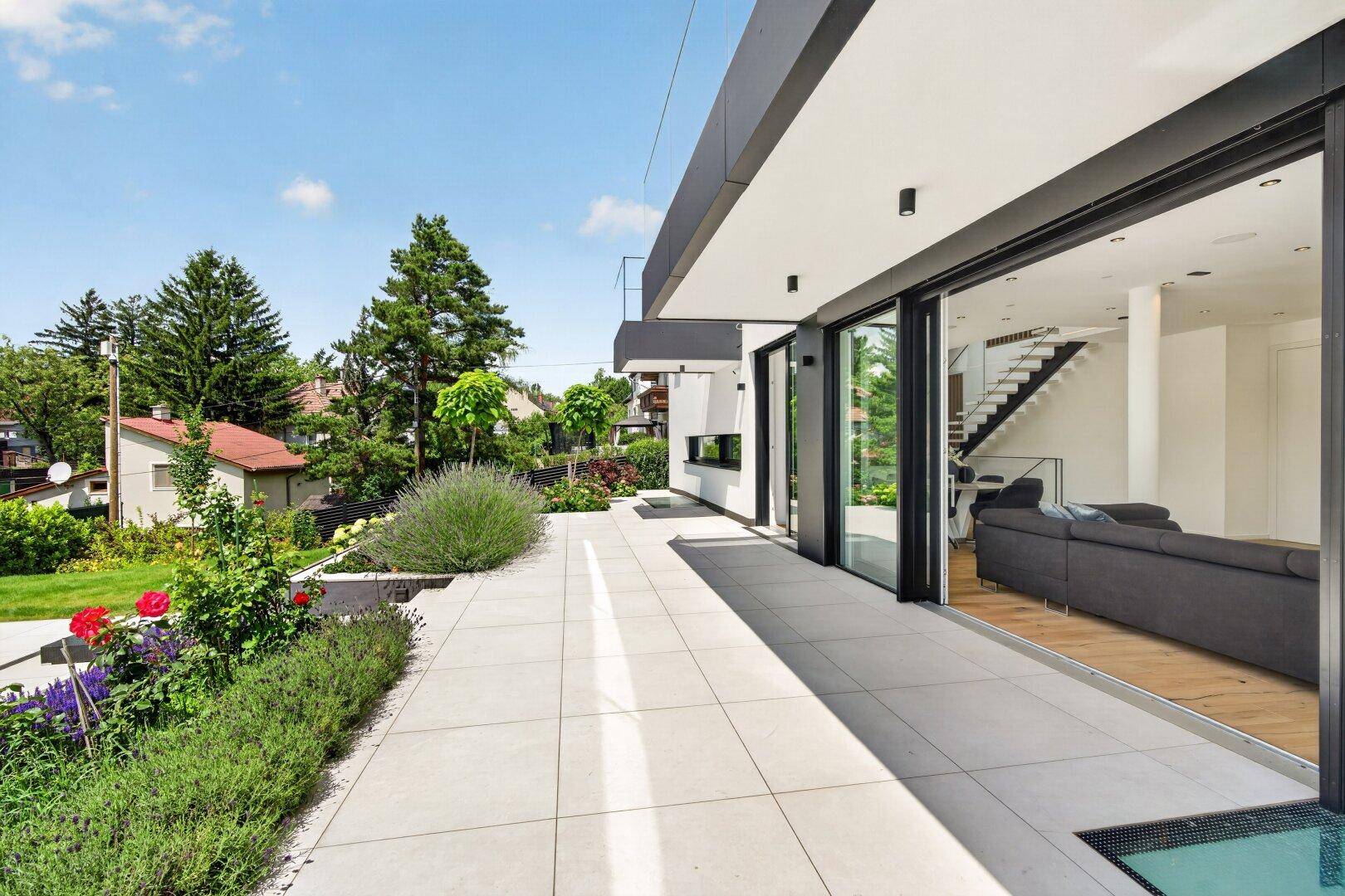 Großzügige, geflieste Terrasse mit Zugang zum Wohnbereich und Blick auf den grünen Garten.