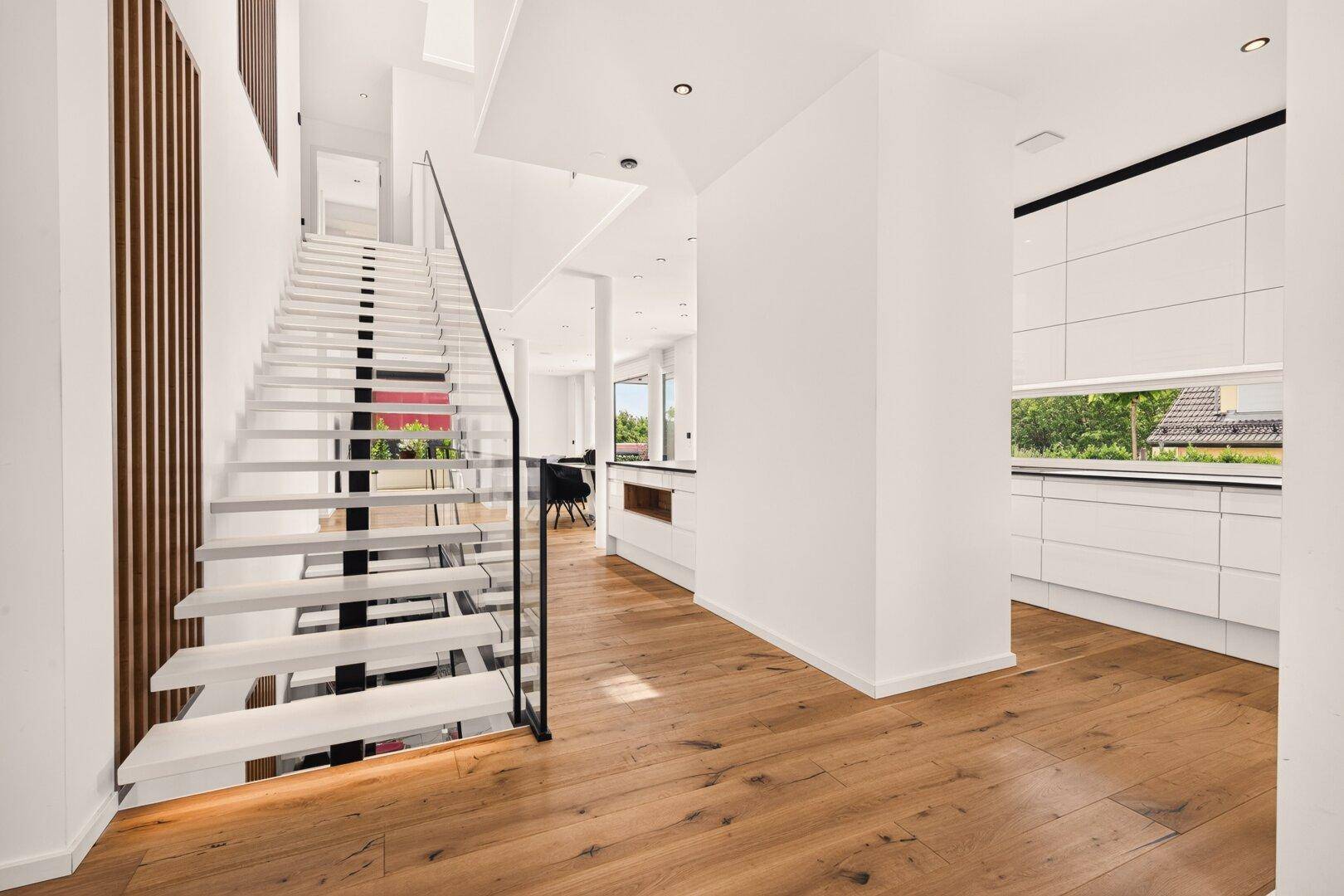 Elegante moderne Treppe mit Glasgeländer und Holzboden, die den offenen Wohnbereich verbindet.