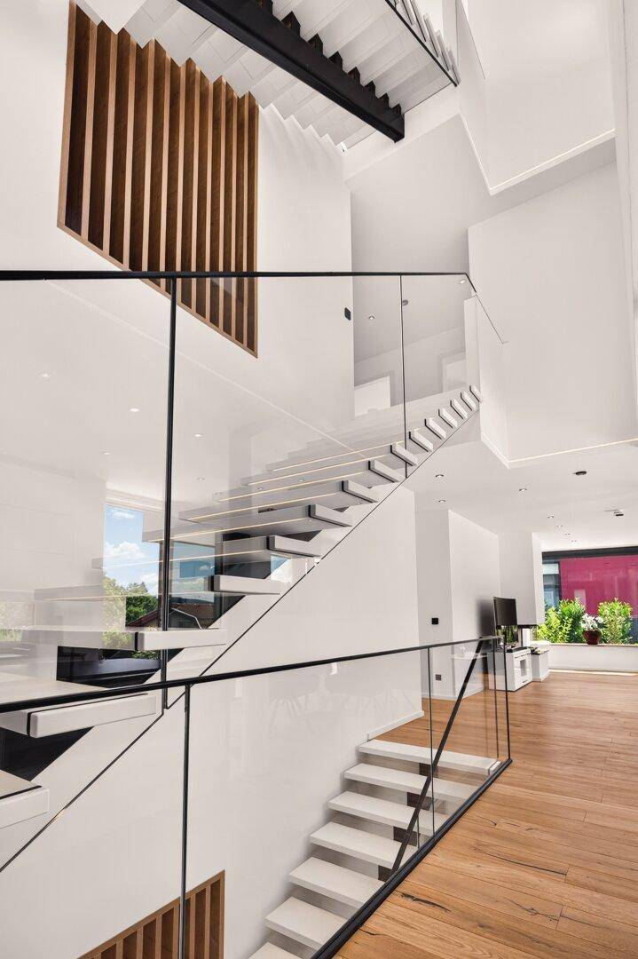 Beeindruckende moderne Treppe mit Glasgeländer, hohen Decken und stilvollen Holzlamellen als Wanddekoration.