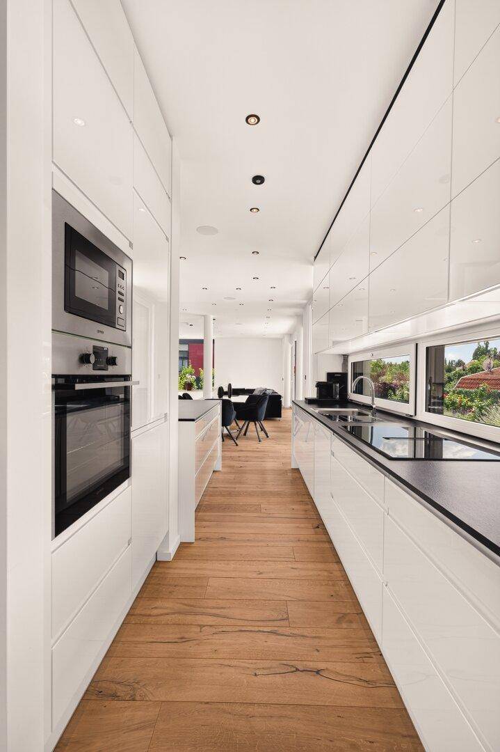 Moderne weiße Küche mit Hochglanzfronten, schwarzen Arbeitsplatten und integrierten Geräten.