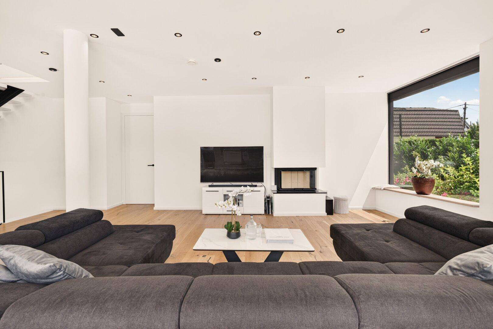 Gemütliches Wohnzimmer mit großem Sofa, modernem Kamin und Holzboden, ideal zum Entspannen.