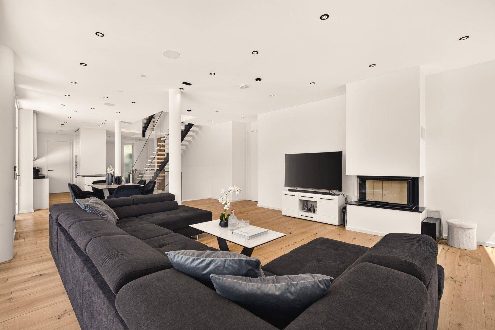 Geräumiges Wohnzimmer mit großem Ecksofa, modernem Kamin und offenem Übergang zu anderen Bereichen.