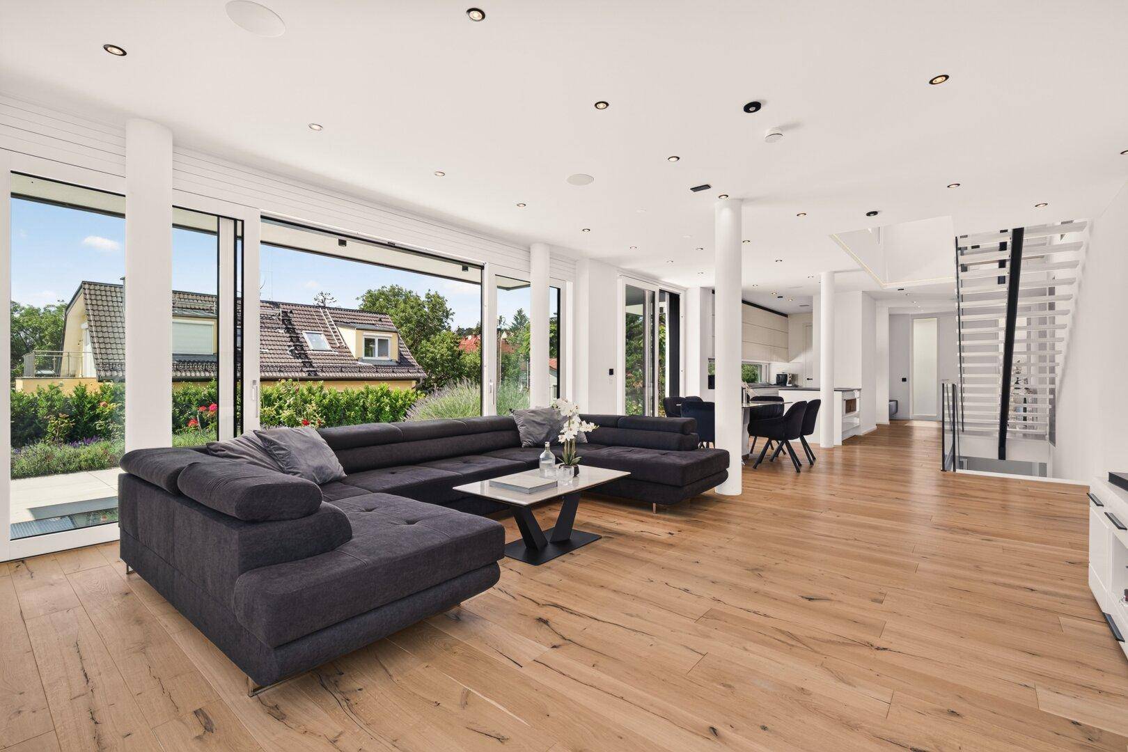 Helles Wohnzimmer mit großem Sofa, Holzboden und raumhohen Schiebetüren zum Außenbereich.