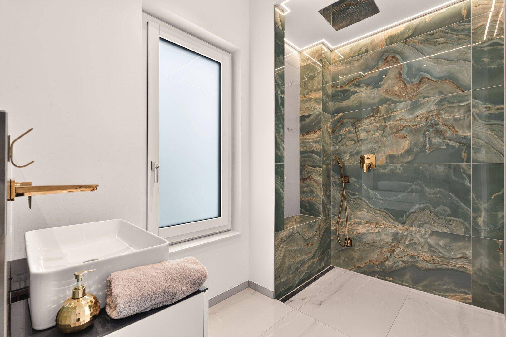 Elegantes Badezimmer mit begehbarer Dusche, grünen Marmorfliesen und Regendusche.