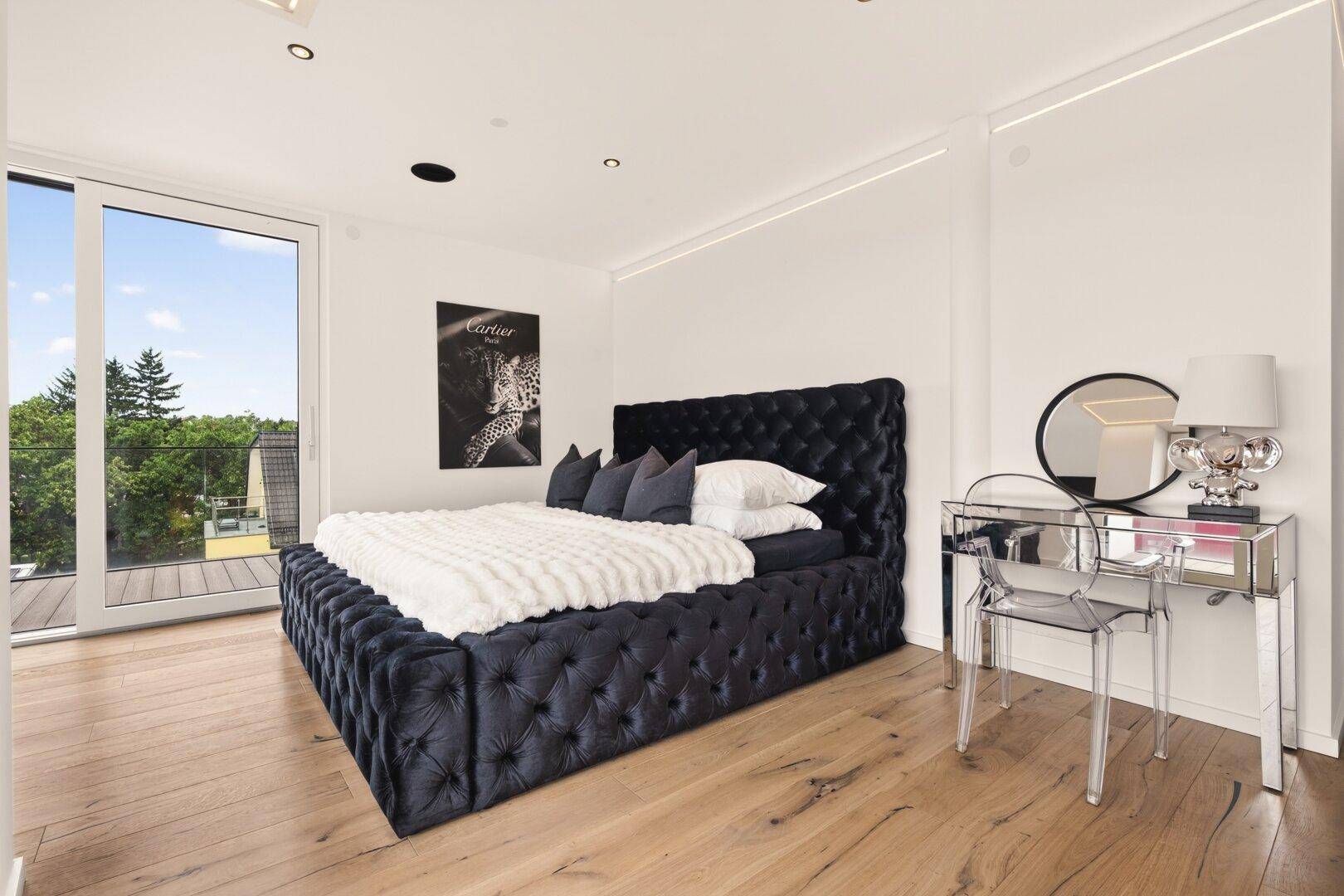 Helles Schlafzimmer mit luxuriösem Samtbett, Holzboden und Zugang zu einem Balkon.