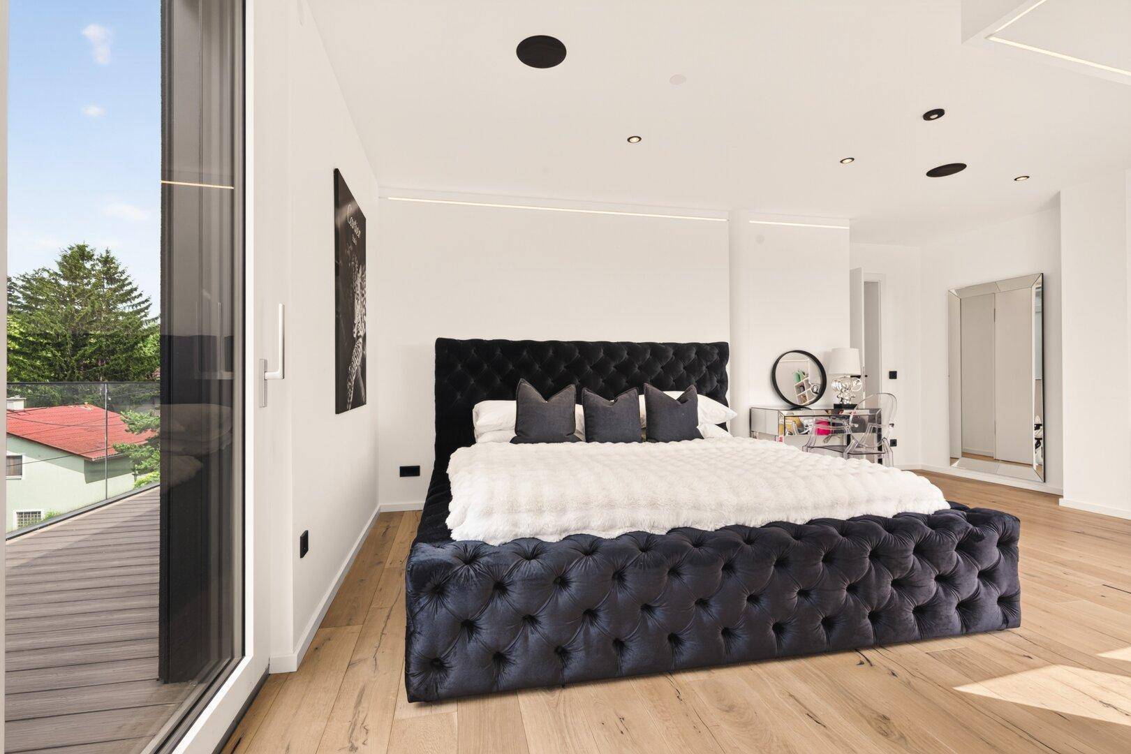 Geräumiges Schlafzimmer mit elegantem Samtbett, Holzboden und viel Tageslicht.