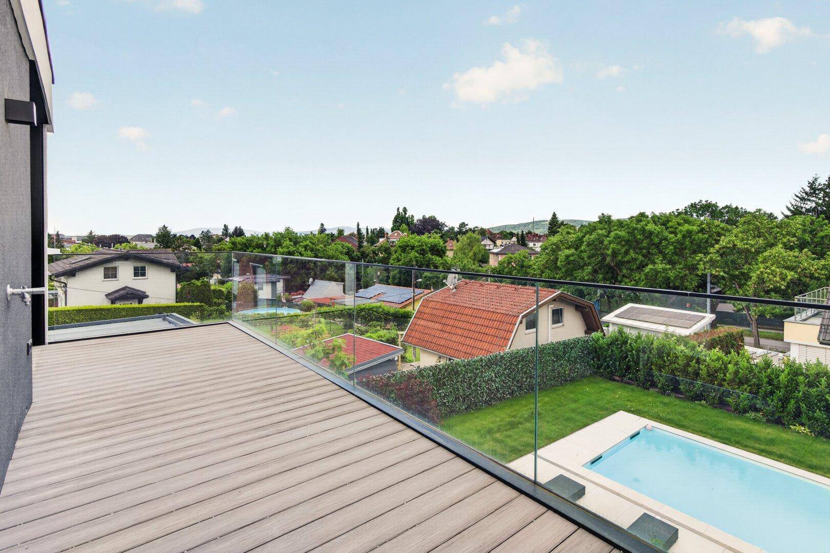 Großer Balkon mit Glasgeländer und weitem Blick über die Umgebung und einen Pool.