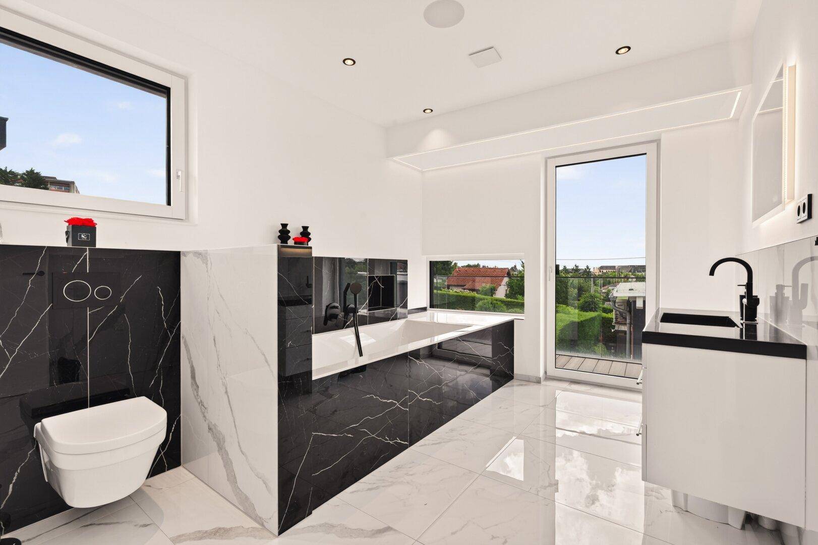 Modernes Badezimmer mit schwarzen Marmorfliesen, Badewanne und großem Fenster mit Ausblick.