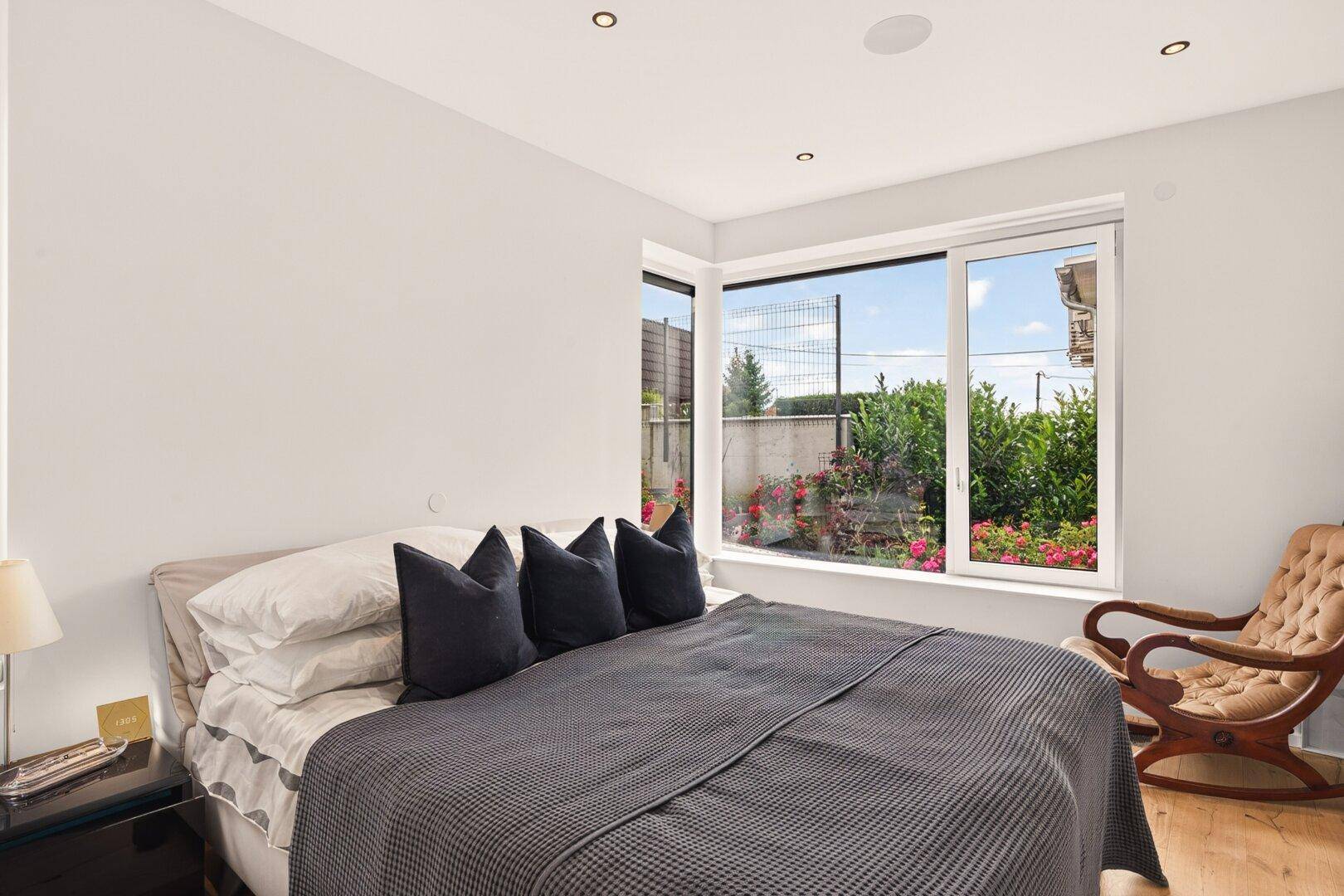 Schlafzimmer mit Holzboden, großem Fenster und Blick auf den Gartenbereich.