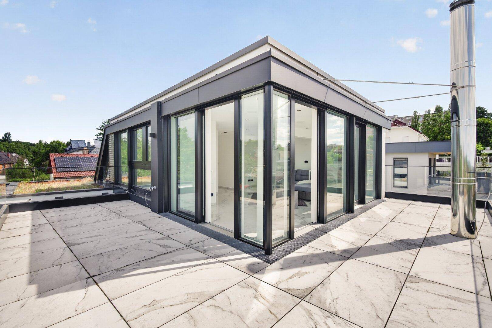 Großzügige Dachterrasse mit Fliesenboden und moderner Glasfassade, die einen weiten Ausblick bietet.